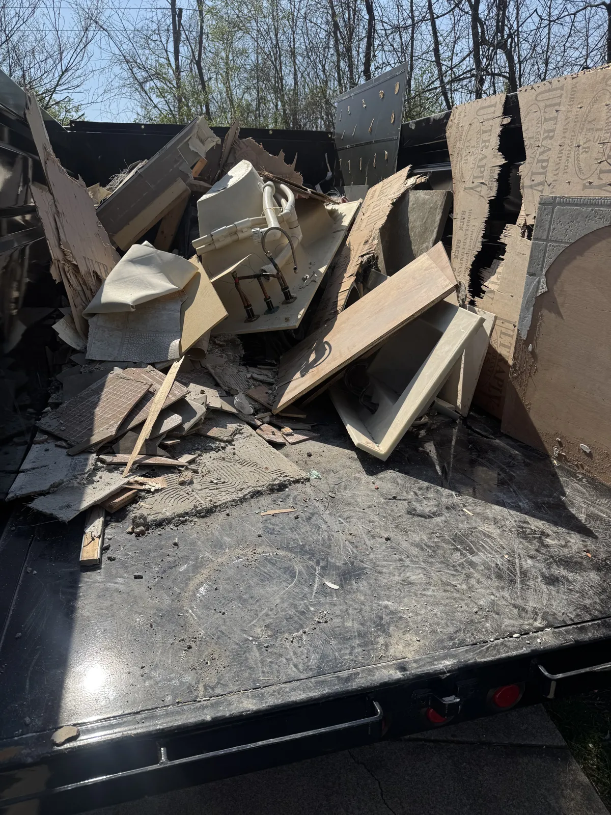 Dump trailer loaded with bathroom remodel debris: tub/shower surround, tile pieces, vanity parts and drywall