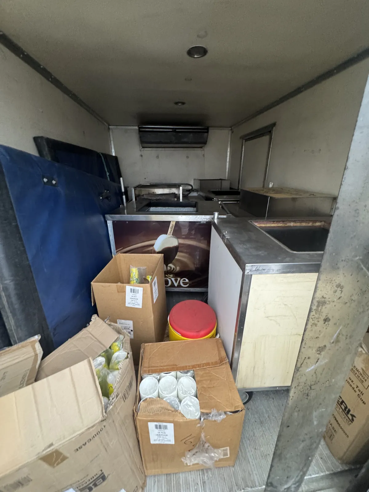 Inside a box truck: ice-cream freezer unit, sink counter, blue mat and boxes of cups (commercial cleanout)