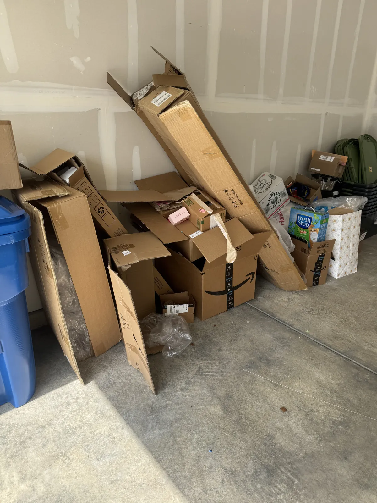 Garage corner piled with broken-down Amazon boxes, packaging and a blue recycling cart