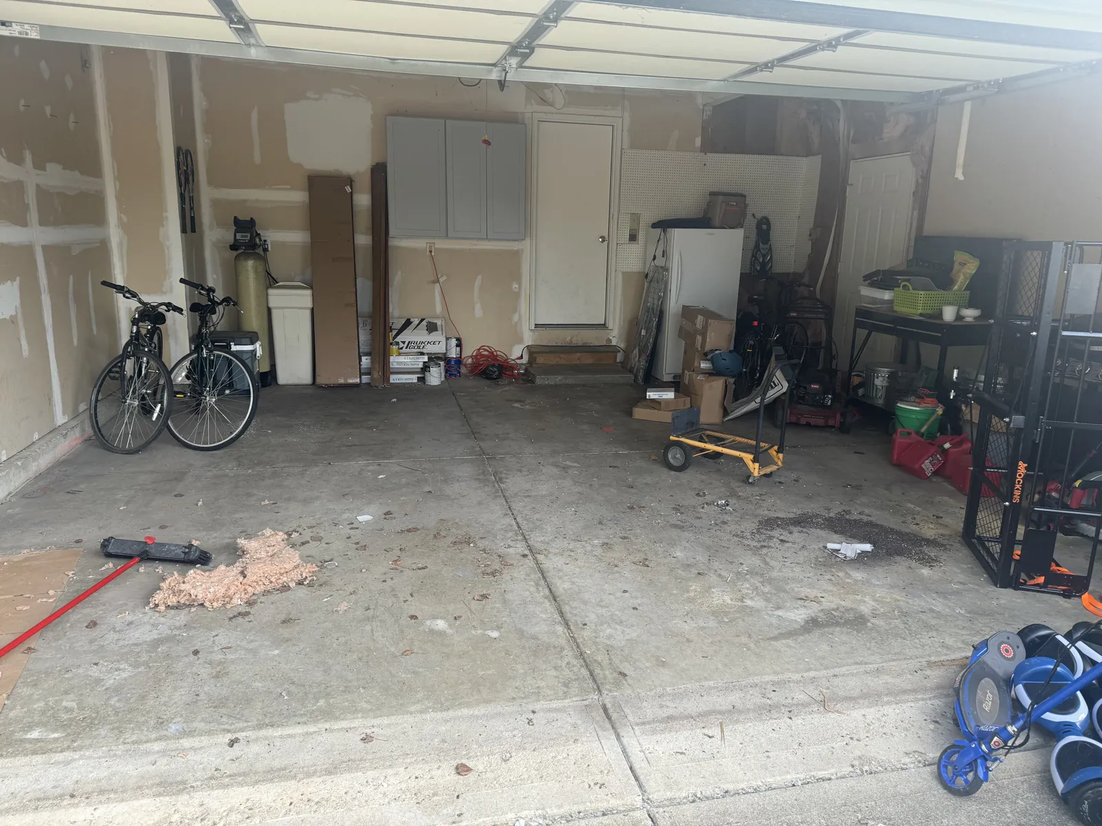 The same garage mostly cleared: two bikes, water softener, fridge and gray cabinets remain
