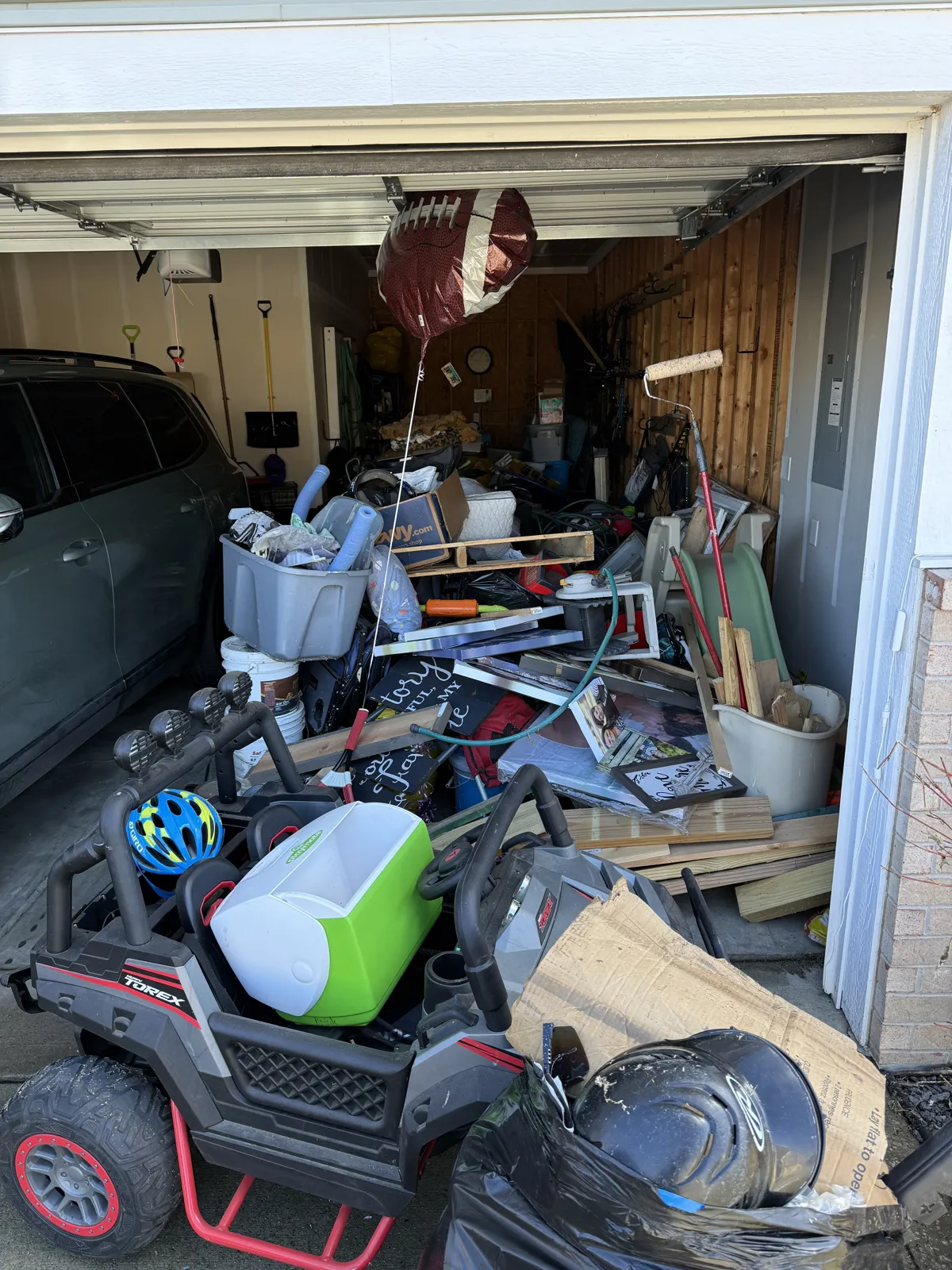 Garage packed floor to ceiling with a kids' ride-on UTV, cooler, lumber, bins, framed pictures and a football