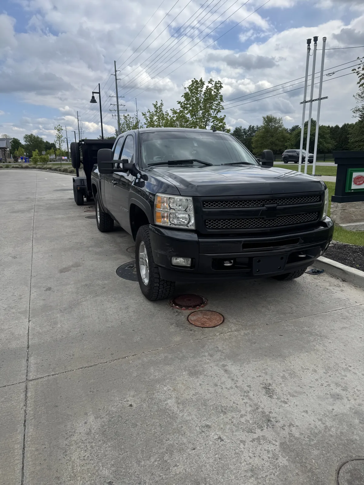 Front three-quarter view of the black pickup with the dump trailer behind, cloudy sky