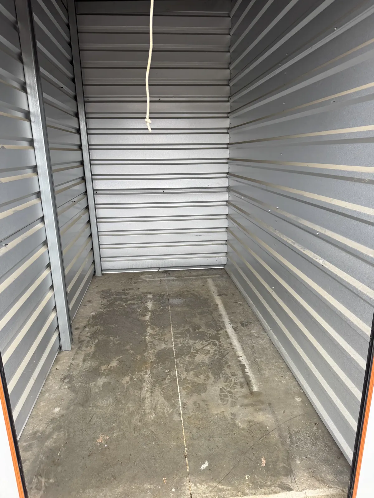 Empty self-storage unit with corrugated metal walls, orange door trim and a pull rope