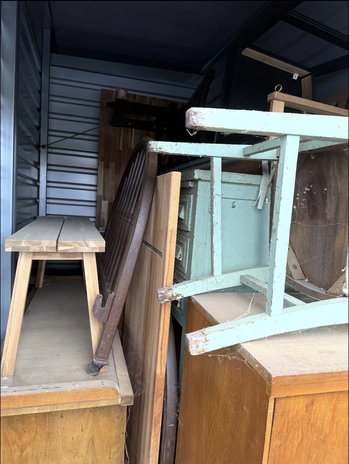 Storage unit packed with old wood furniture: bench, painted green chest and chair, dresser, round table top