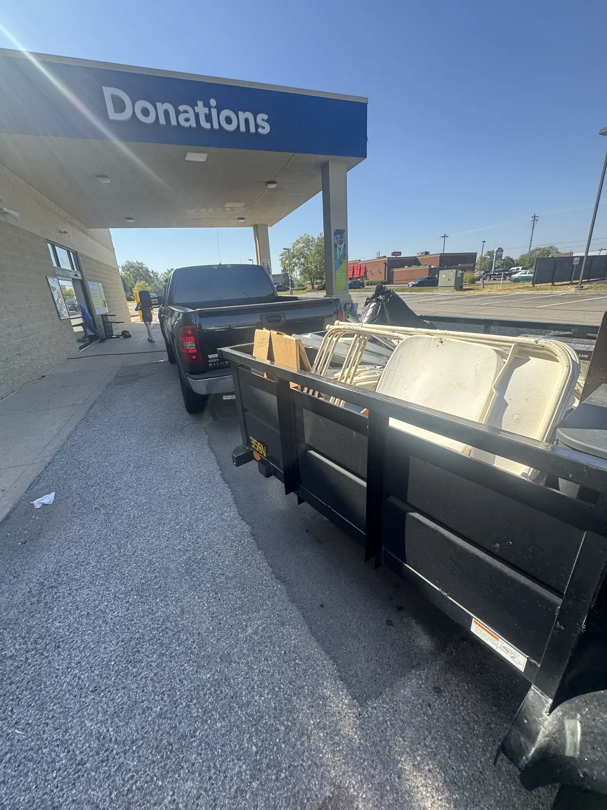 Black utility trailer loaded with folding chairs and boxes, hitched to a black pickup under a blue